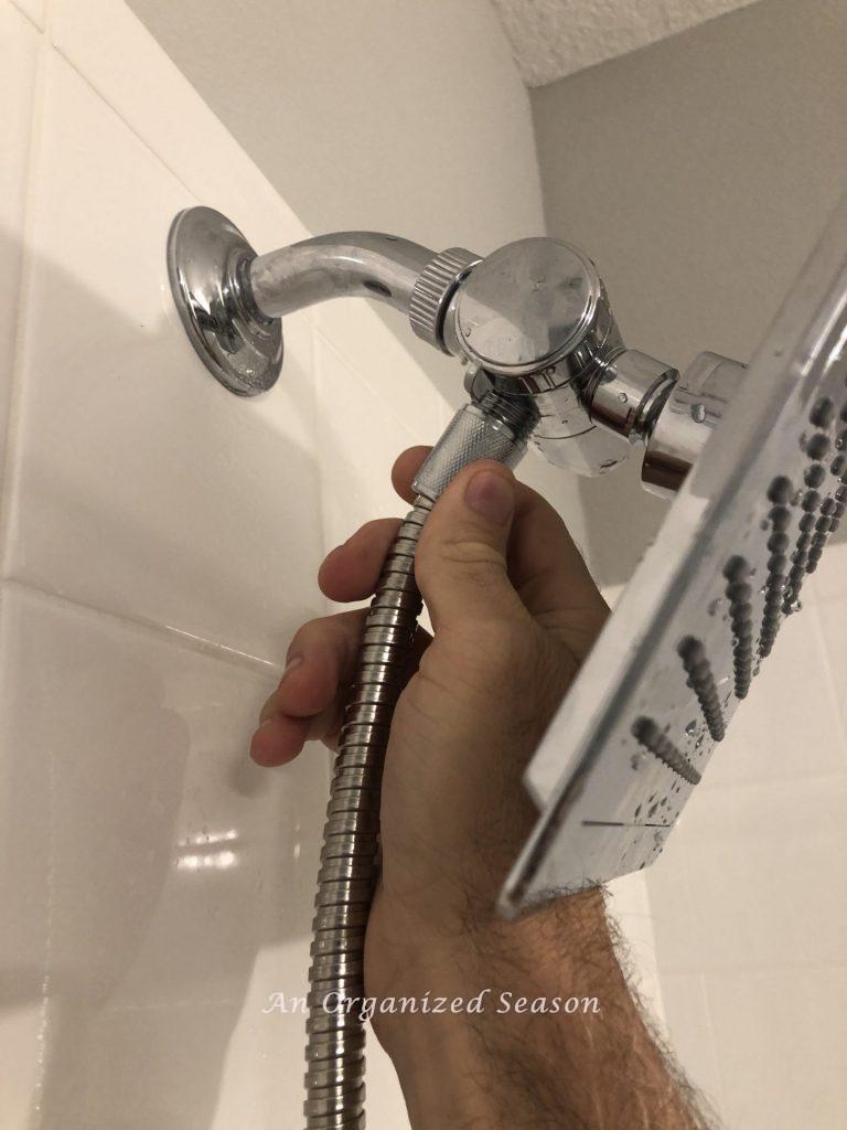 A man screwing a hose into a shower head showing a step to easily install a new shower head.