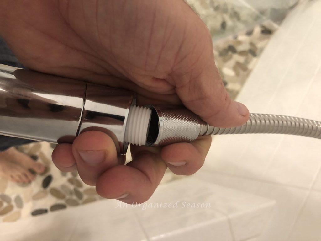 A man screwing a hand held shower into a hose showing a step to easily install a new shower head.