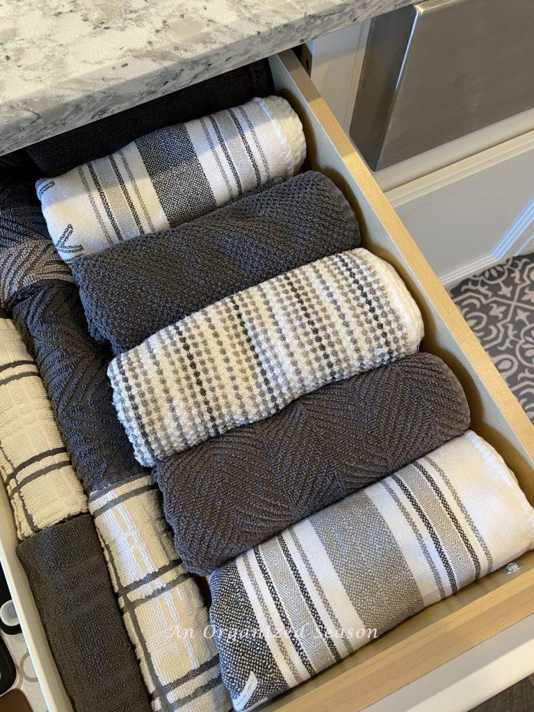 How to organize gray and white kitchen towels and dishcloths in a kitchen drawer. 
