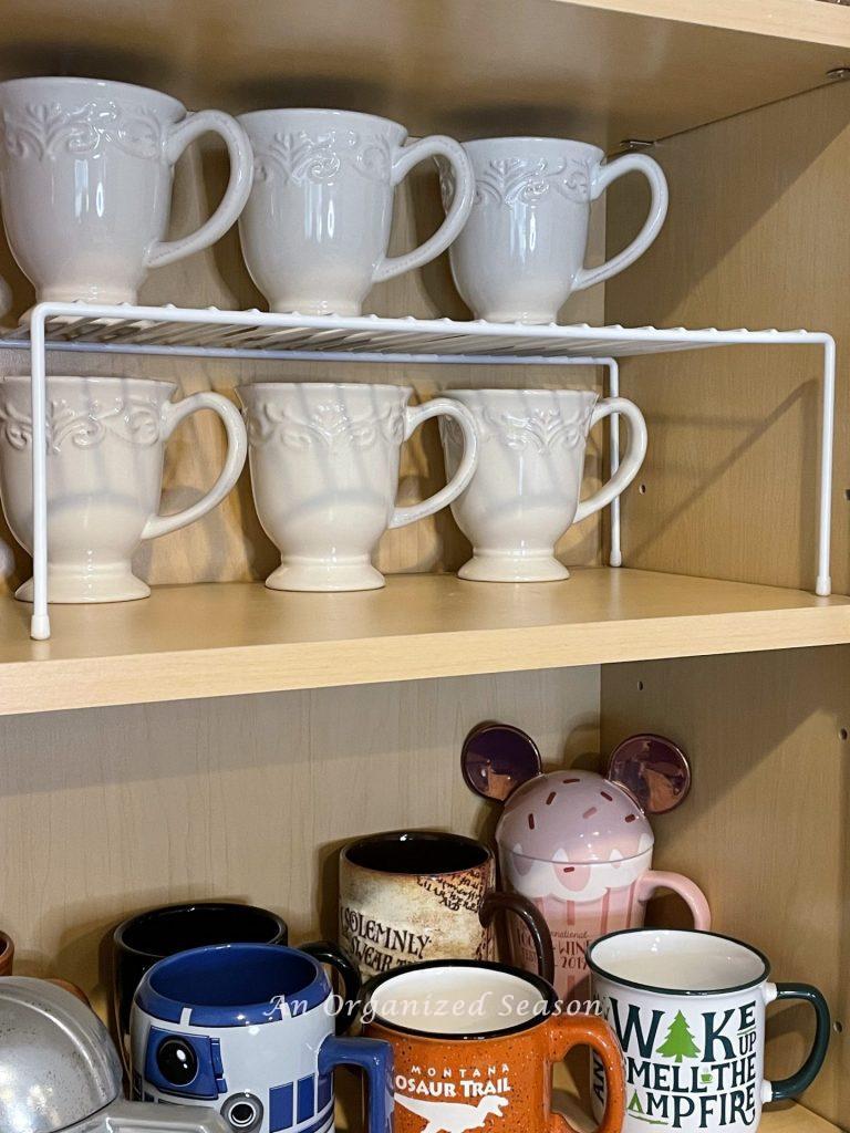 A white wire shelf which doubles the storage space for coffee cups is a helpful kitchen cabinet organization solution. 