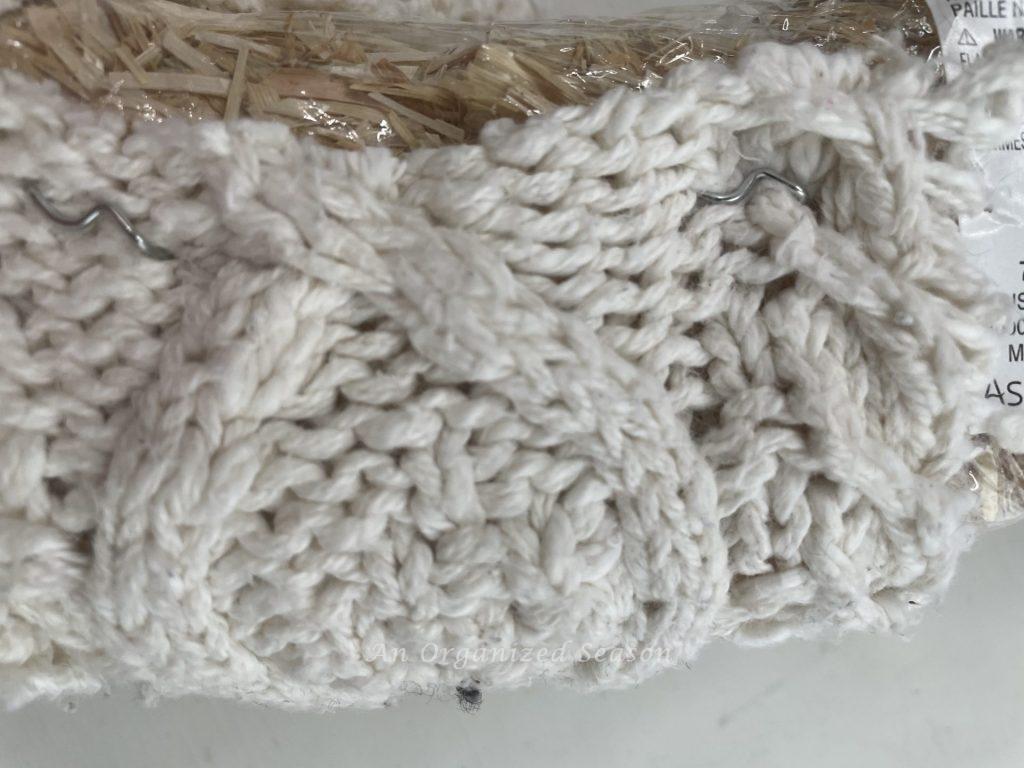 A strip of a winter sweater that has been attached to a wreath with floral picks. 
