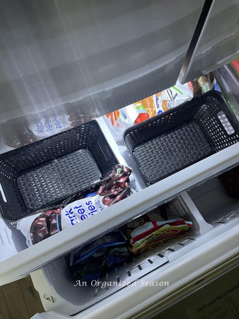 Black plastic baskets place in a freezer to organize frozen food. 