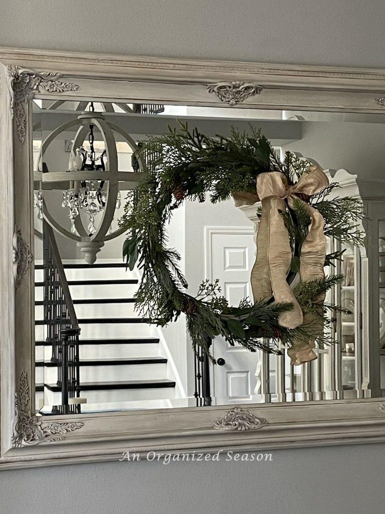 An evergreen wreath with gold bow hanging on a mirror to decorate a home for Winter. 