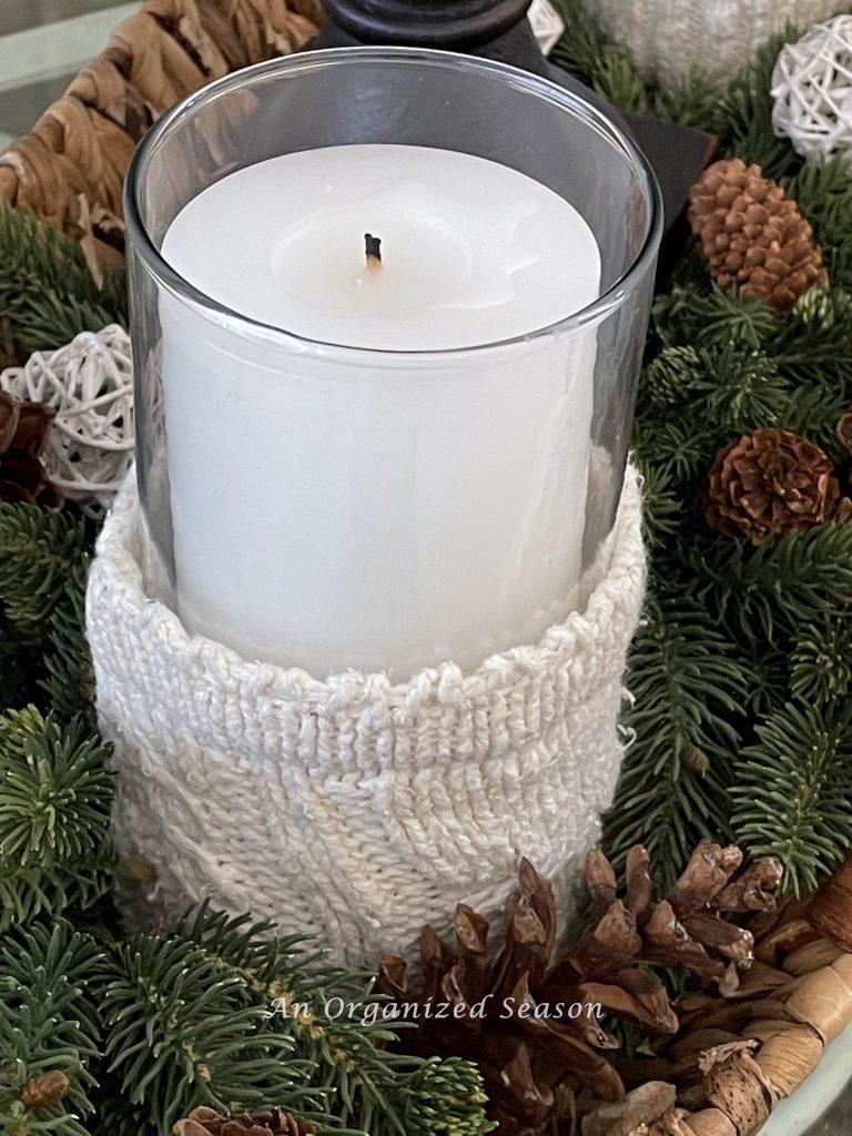 A white candle inside a glass vase covered with a sweater sleeve showing how to decorate a home for Winter. 