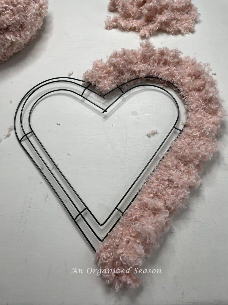 Teddy Bear yarn that has been looped around half of a heart wreath form showing how to craft a Teddy Bear yarn heart.