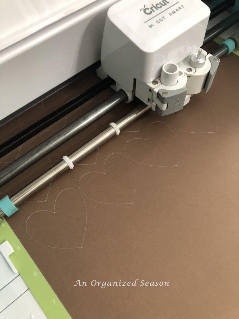 A Cricut machine cutting out brown hearts to make a paper heart and ribbon garland.