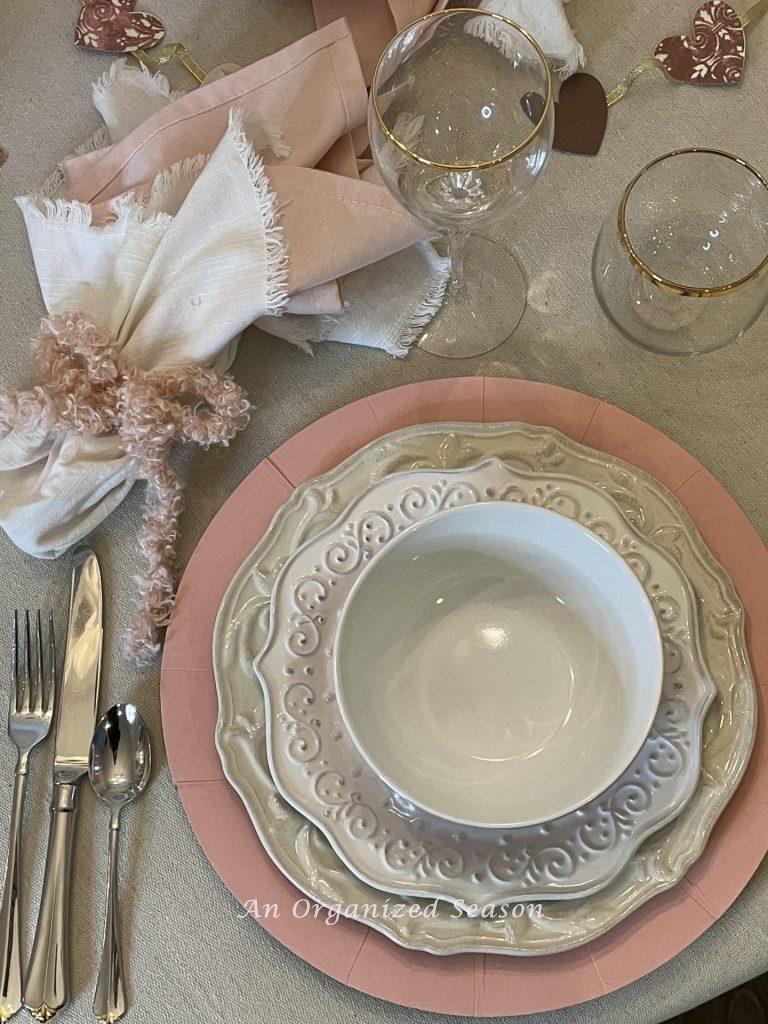 Table decor for Valentine's Day with a place setting of pink charger, white plates with glasses trimmed in gold. 