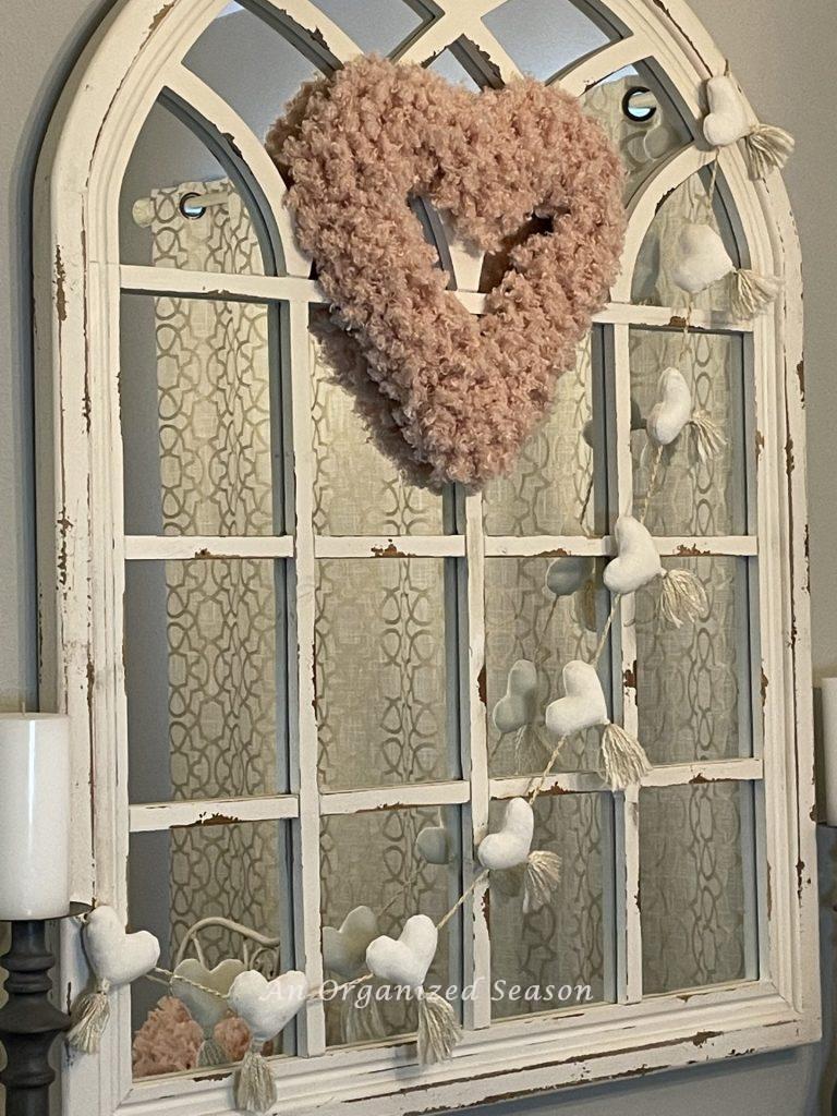 A pink yarn heart displayed on a mirror to coordinate with the table decor for Valentine's Day.