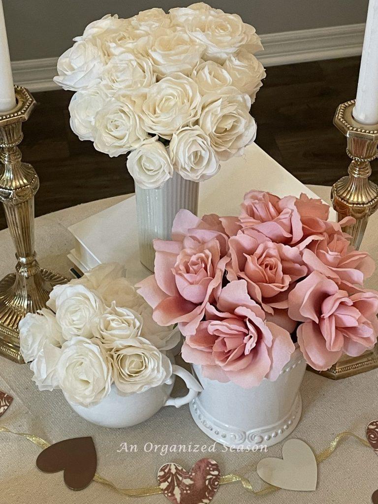 Two white vases filled with  white roses and one white vase filled with pink roses displaying table decor for Valentine's Day.