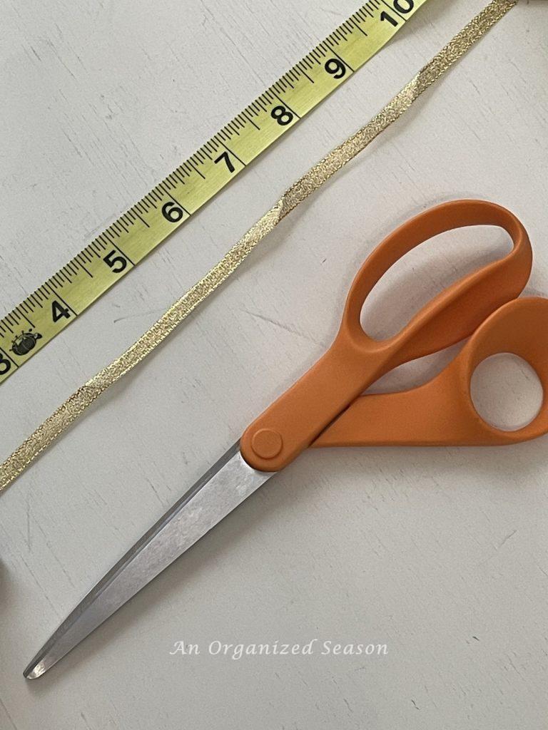 A measuring tape, gold ribbon, and scissors used to make a paper heart and ribbon garland.
