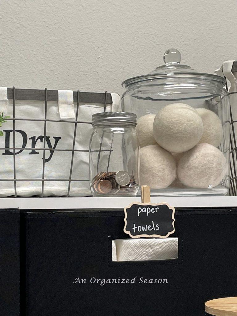 A cookie jar holding dryer balls and a mason jar holding change on a shelf in a laundry room showing practical laundry room organization ideas.