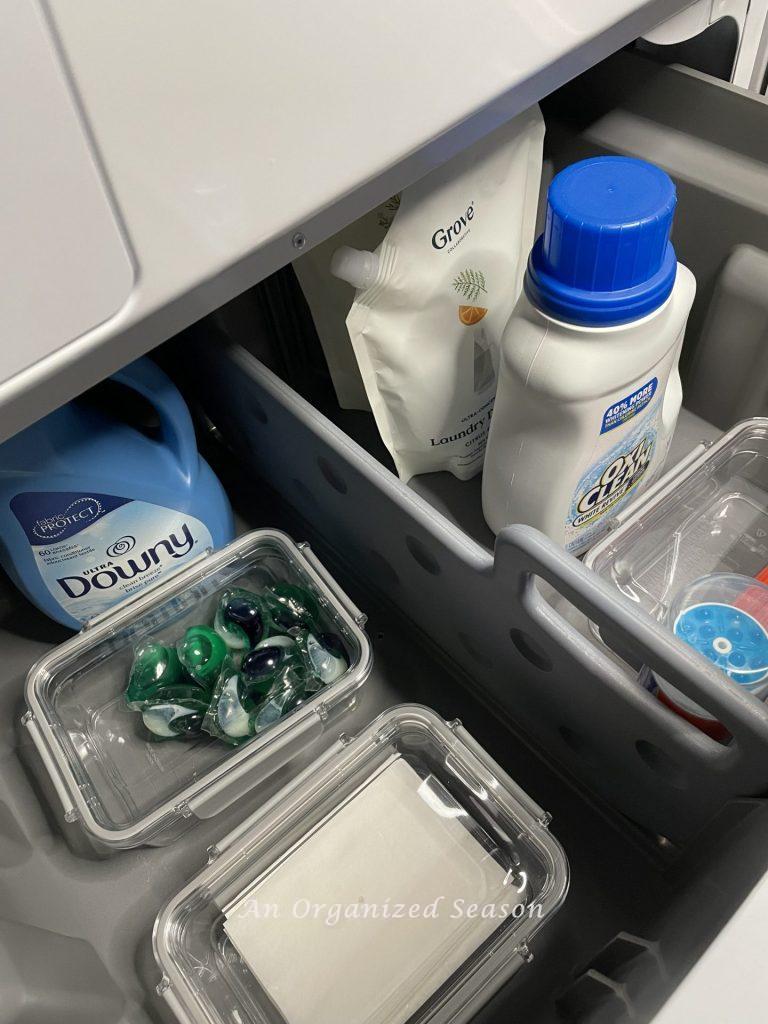 An open  pedestal drawer under a washing machine with organized laundry detergents showing practical laundry room organization ideas.
