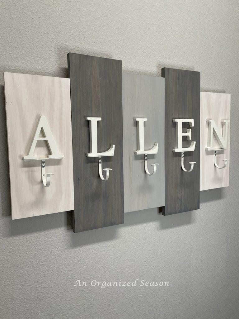 A coat rack with letters spelling the name "Allen" hanging on a laundry room wall showing practical laundry room organization ideas