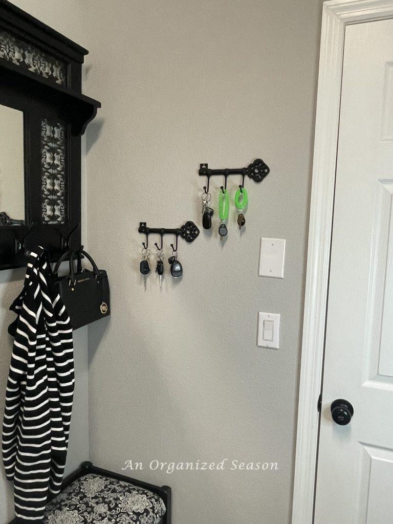 Two lack metal key holders hanging next to a coat rack in a laundry room showing practical laundry room organization ideas.