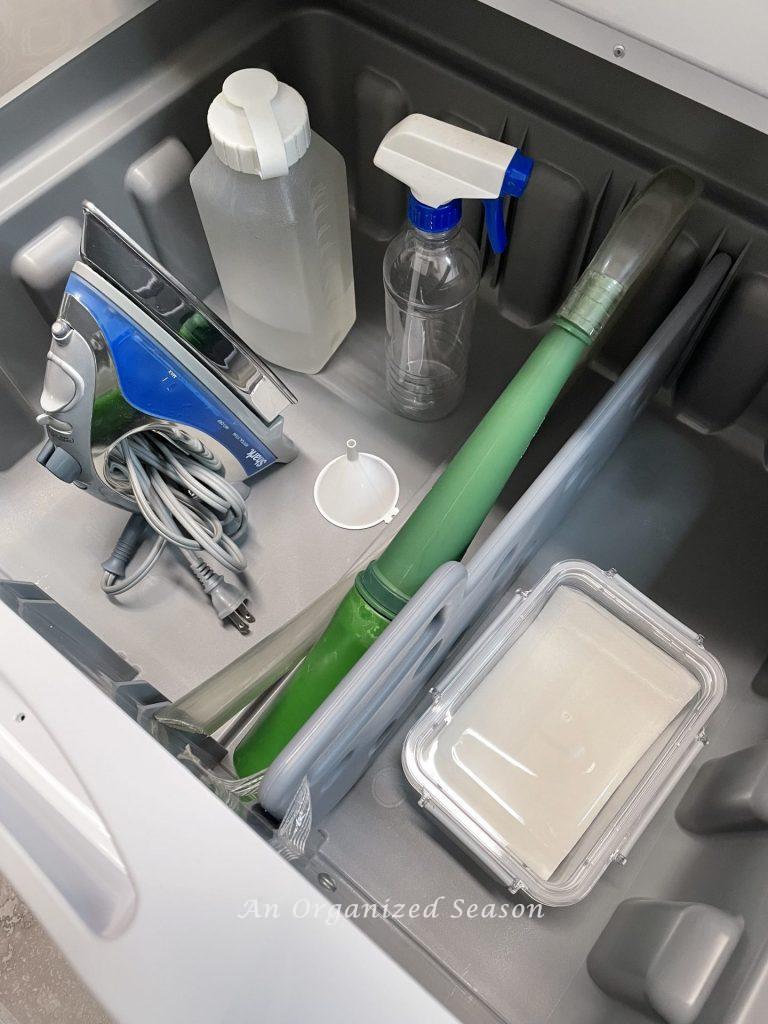 An open  pedestal drawer under a dryer with organized laundry items showing practical laundry room organization ideas.