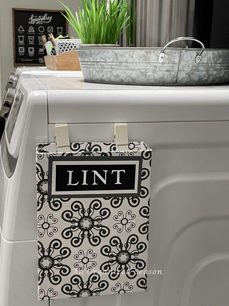 A lint box hanging on the side of a dryer showing  practical laundry room organization ideas.
