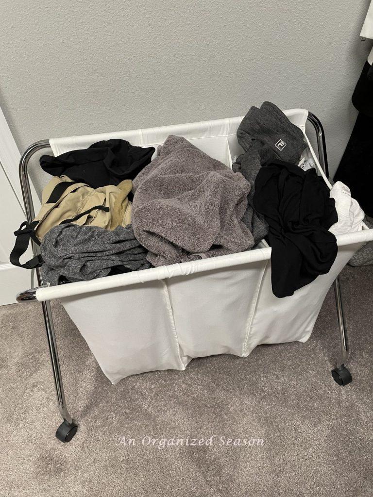 A clothe laundry hamper with three sections filled to the top with dirty clothes. Showing how to simplify the chore of laundry.