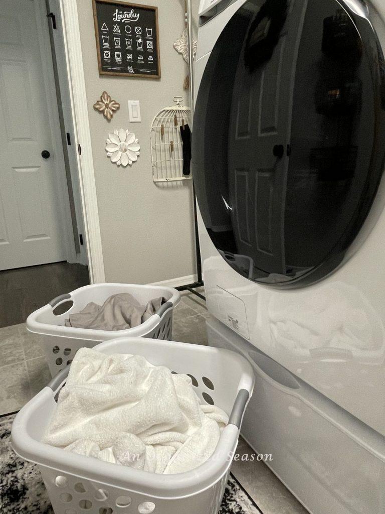 A washing machine with two baskets of dirty laundry in front of it. Showing how to simplify the chore of laundry.