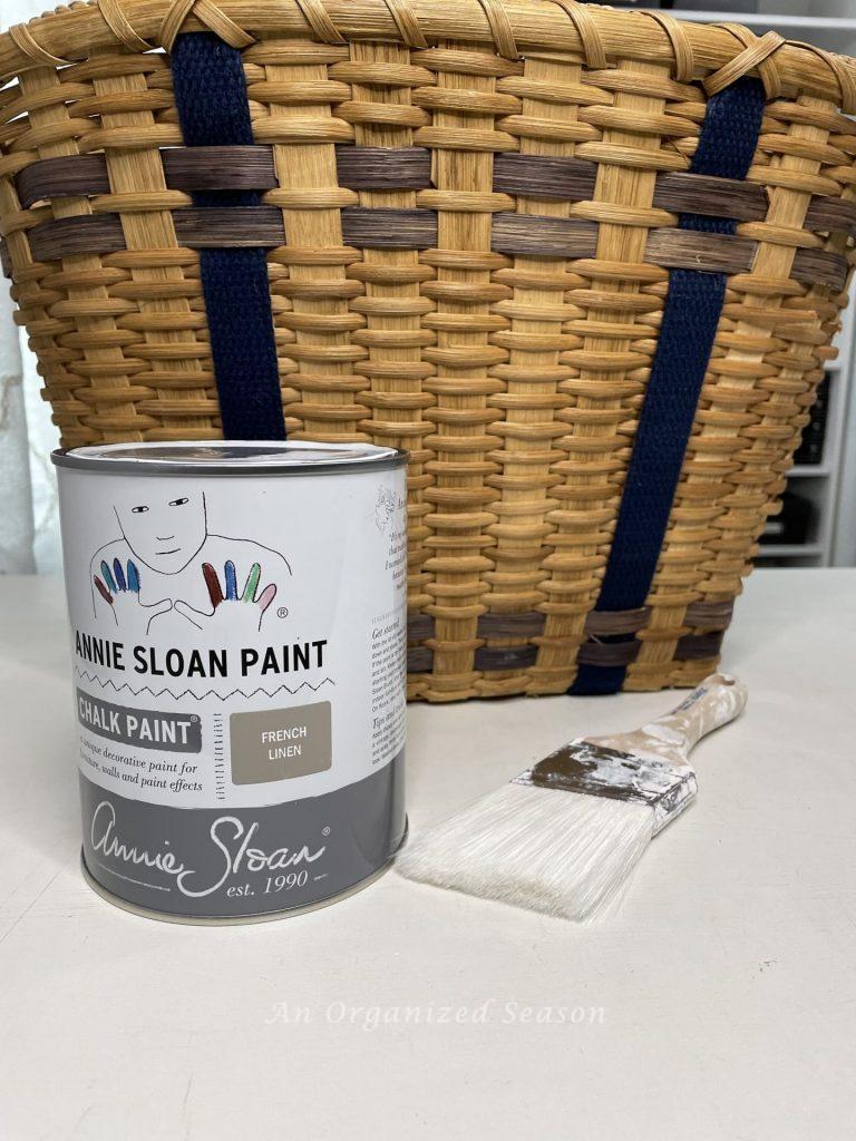 A basket, can of chalk paint, and a paintbrush needed to make a floral basket wreath.