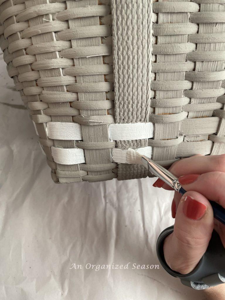 A woman's hand painting white stripes on a basket, step two to make a floral basket wreath.