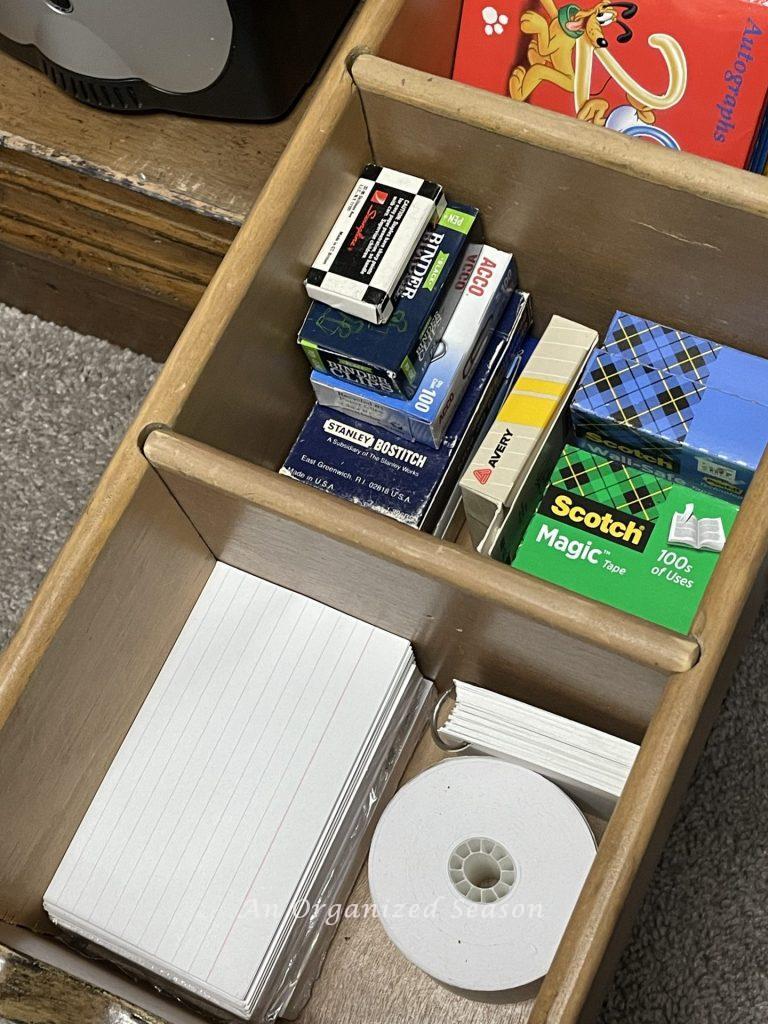 A desk drawer with dividers separating index cards and boxes of staples and tape, an example of ideas to organize a desk.