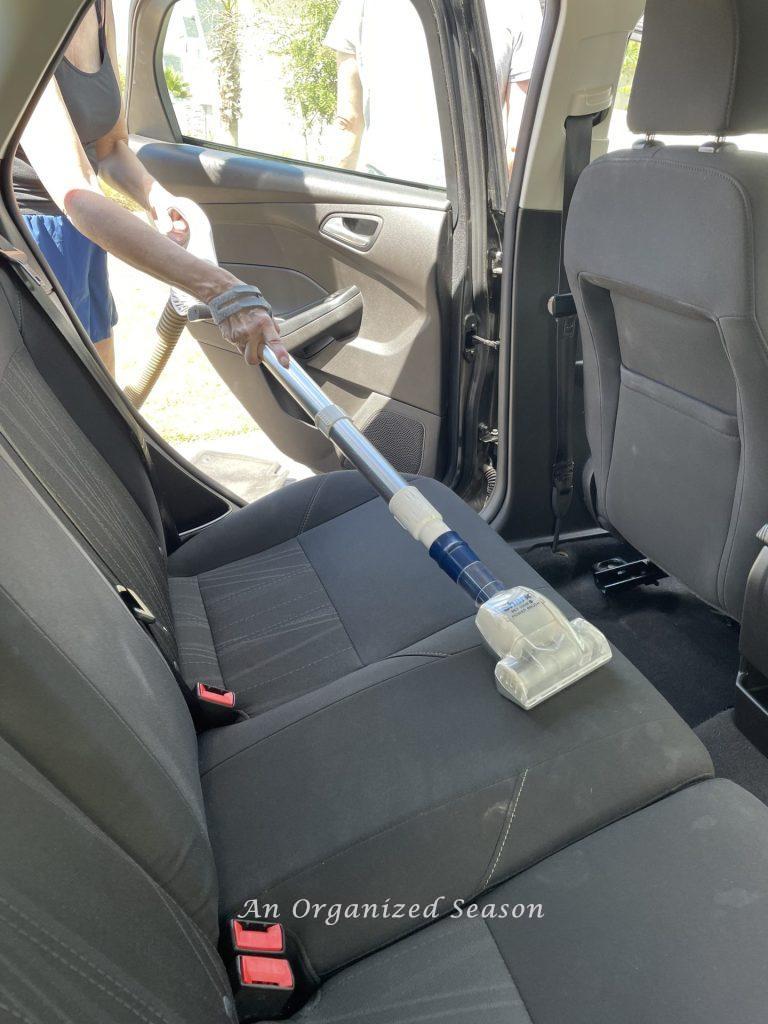 Someone vacuuming the back seat of a car, showing a strategy to clean and organize a car.