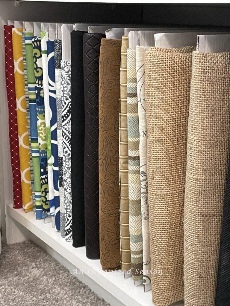 Different fabrics wrapped around pieces of cardboard and displayed on a bookshelf. showing ideas to organize a craft space.