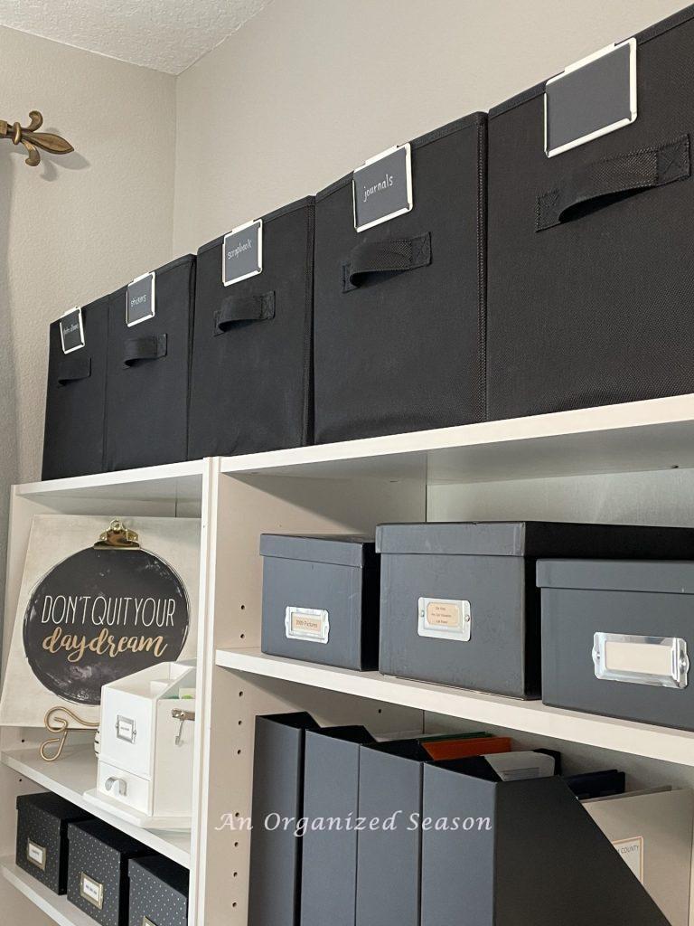 Five black fabric cube bines sitting on top a book shelf showing ideas to organize a craft space.