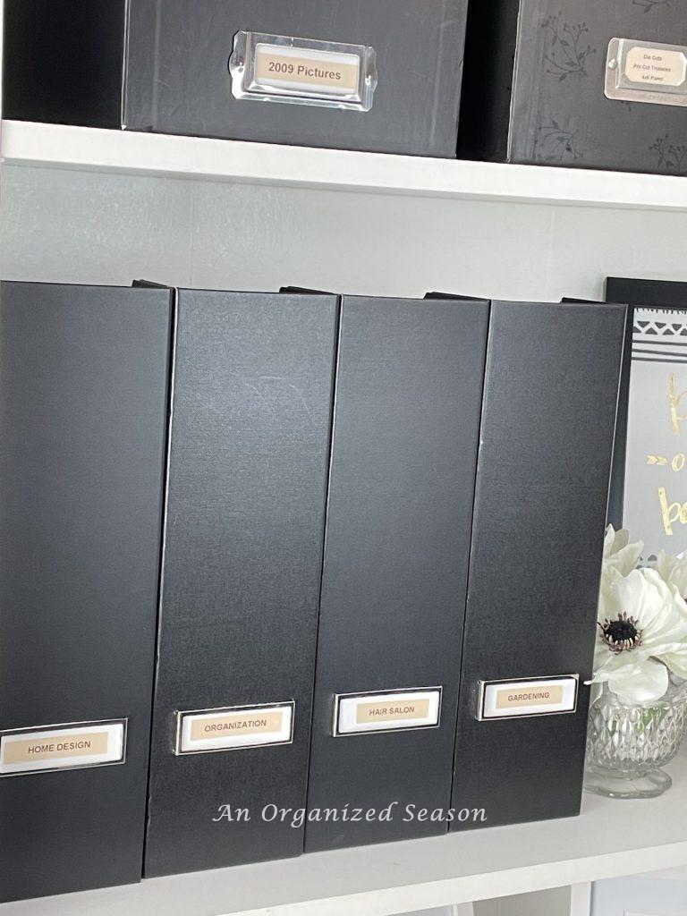 Four black magazine holders sitting on a bookshelf, showing ideas to organize a craft space. 