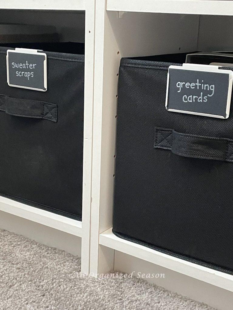 Two black storage cubes with white and black clip-on labels, showing ideas to organize a craft space.