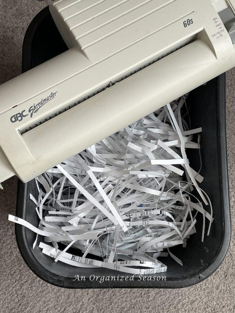 A trash can with a shredder that's full of shredded paper, showing how to get rid of paper clutter.