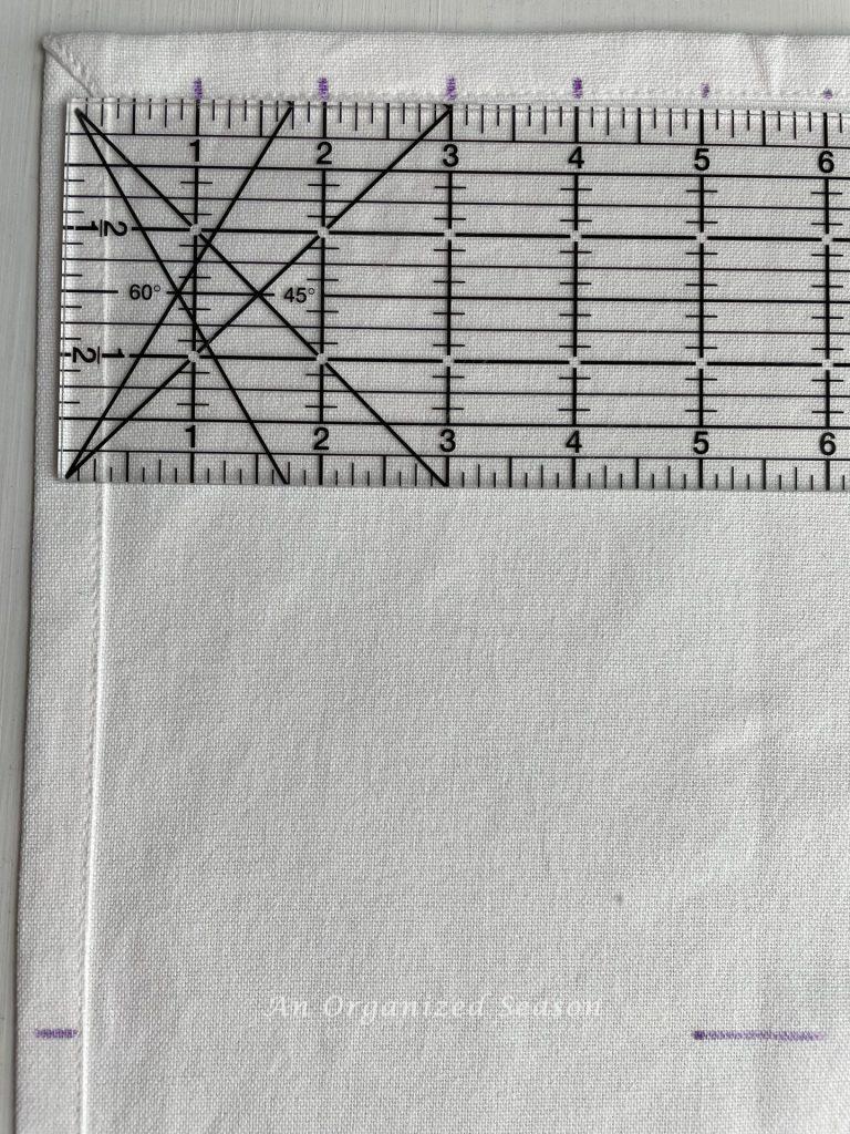 A ruler on top of a dish towel with one-inch marks that will be used to make a no-sew dish towel pillow.