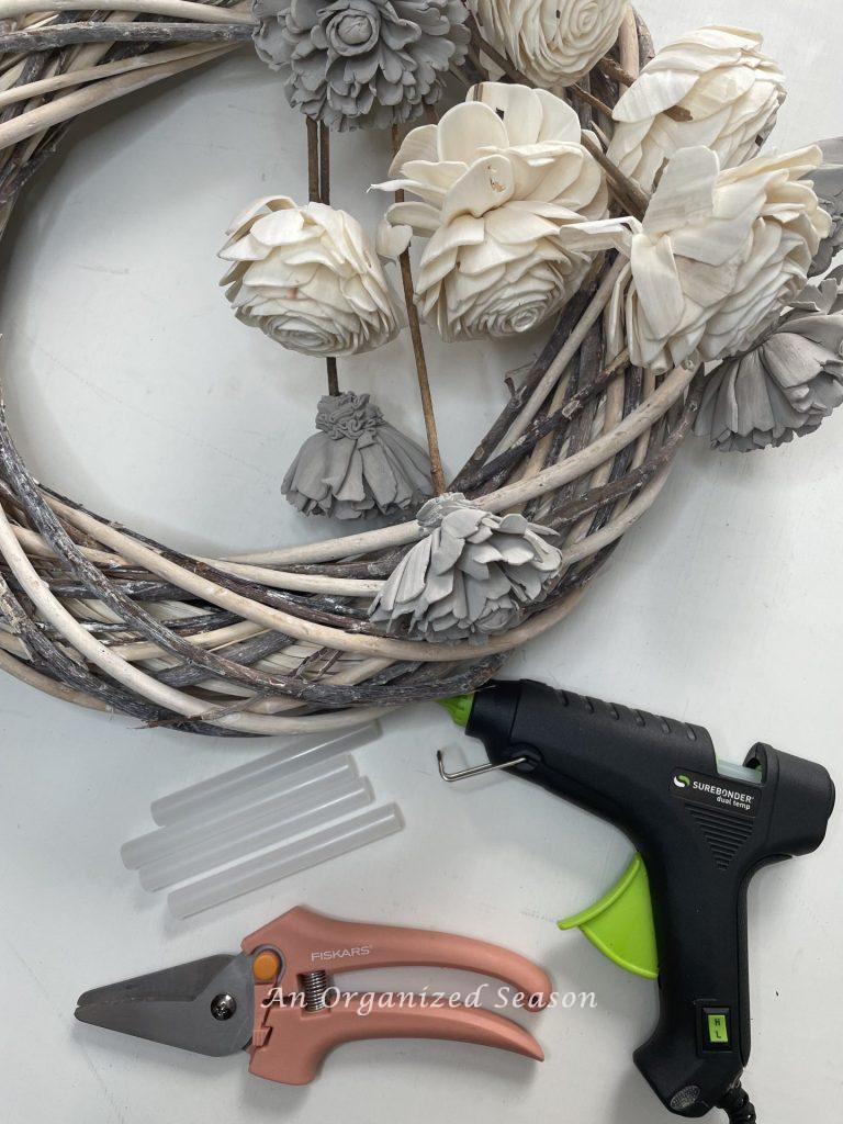 Wreath, flowers, glue gun, and pruners are the items needed to  create a wood flower wreath.