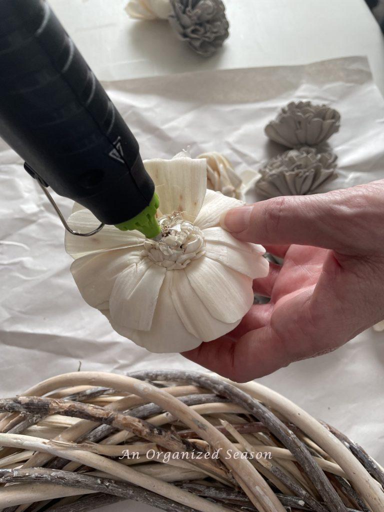 A woman putting hot glue on the back of a flower that will go on a wood flower wreath.