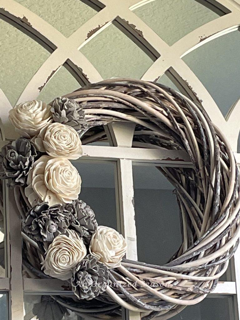 A gray and white wood flower wreath hanging on a mirror.