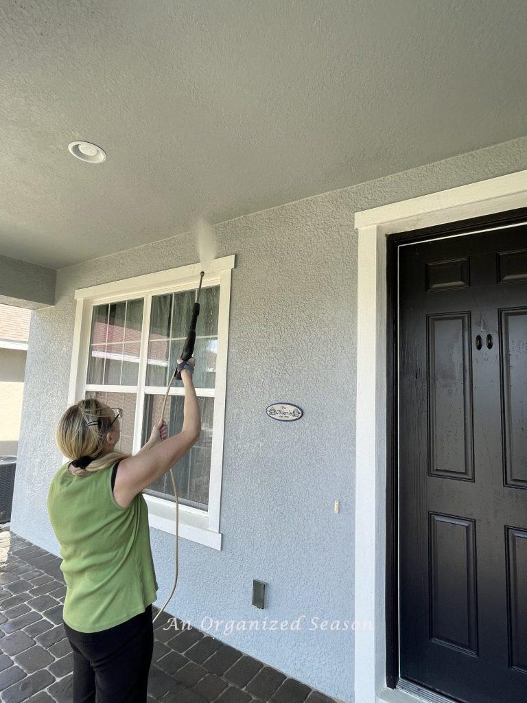 A woman spring cleans her porch with a power washer.