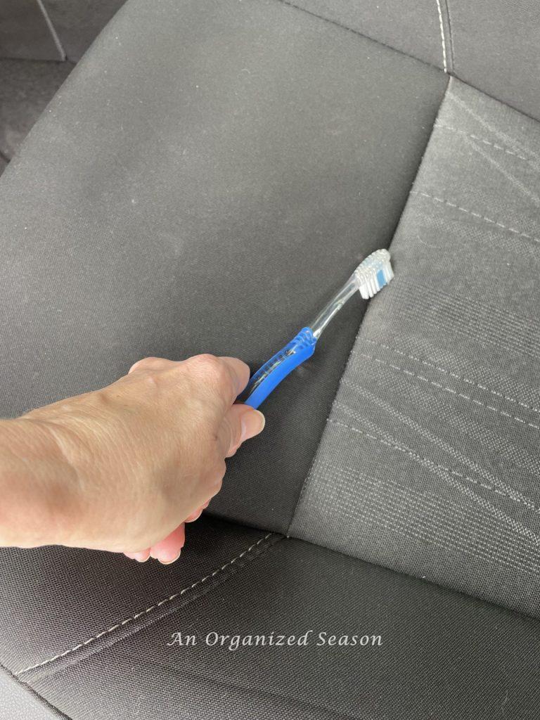A toothbrush cleaning dirt from a car seat showing a strategy to clean and organize a car. 