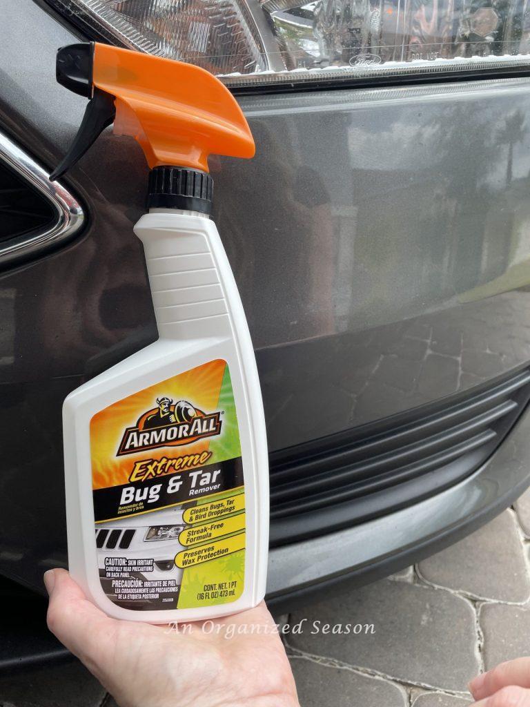 Someone holding a bottle of Armor All Bug & Tar remover in front of a car. A product used as a strategy to clean and organize a car.
