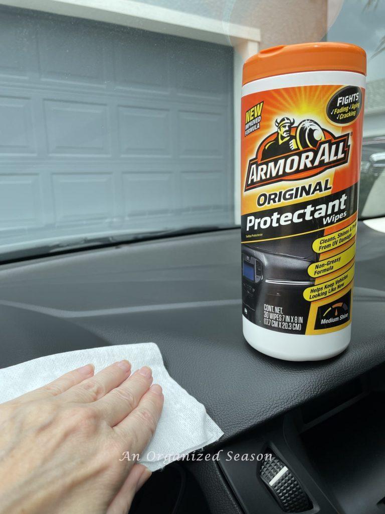 A bottle of Armor All Protectant Wipes sitting on a car dashboard and a hand using one to clean the car, part of the strategy to clean and organize a car.