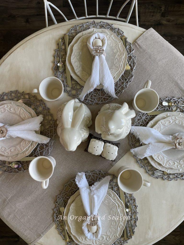 A table with four place settings and two bunnies as a centerpiece, showing ideas to decorate your home for Spring. 