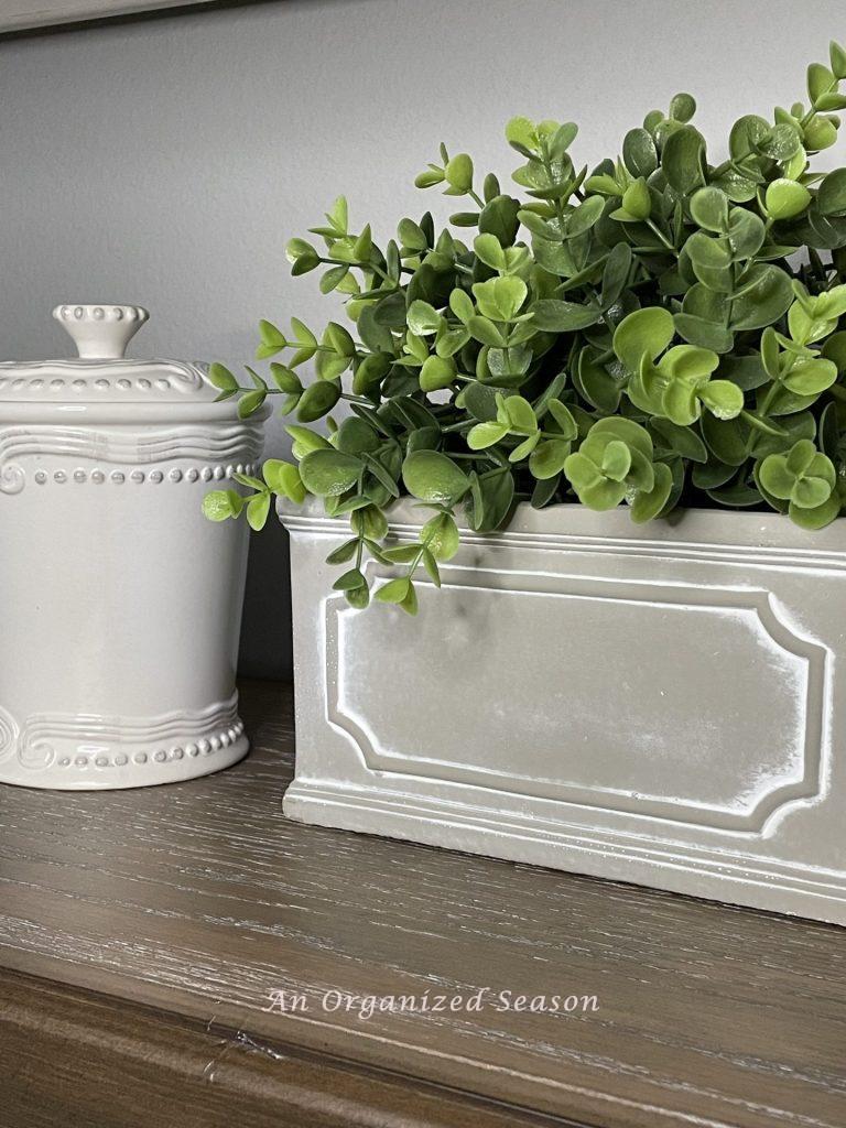 A white canister and topiary are an example of ideas to decorate your home for Spring.