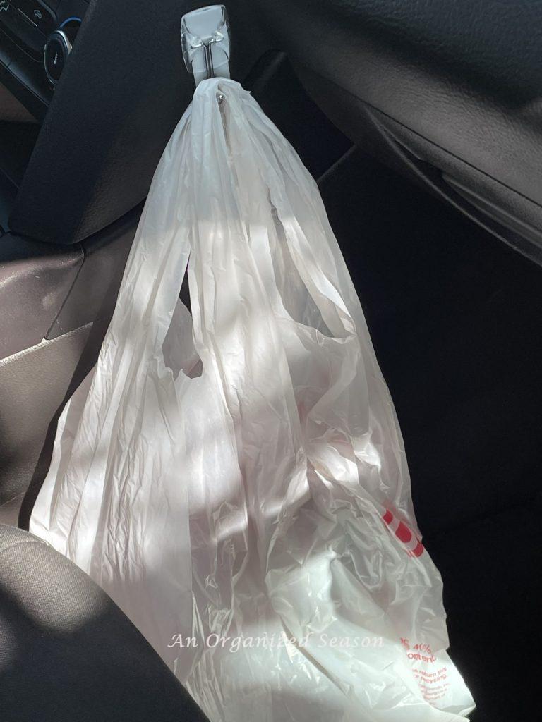 A command hook attached to inside of car and holding a plastic trash bag is an example of a  strategy to clean and organize a car.