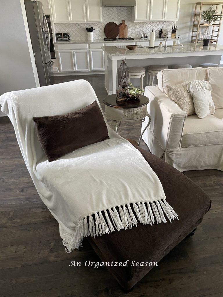 A white fringed throw blanket draped on a brown chaise lounge, showing ideas to decorate your home for Spring.