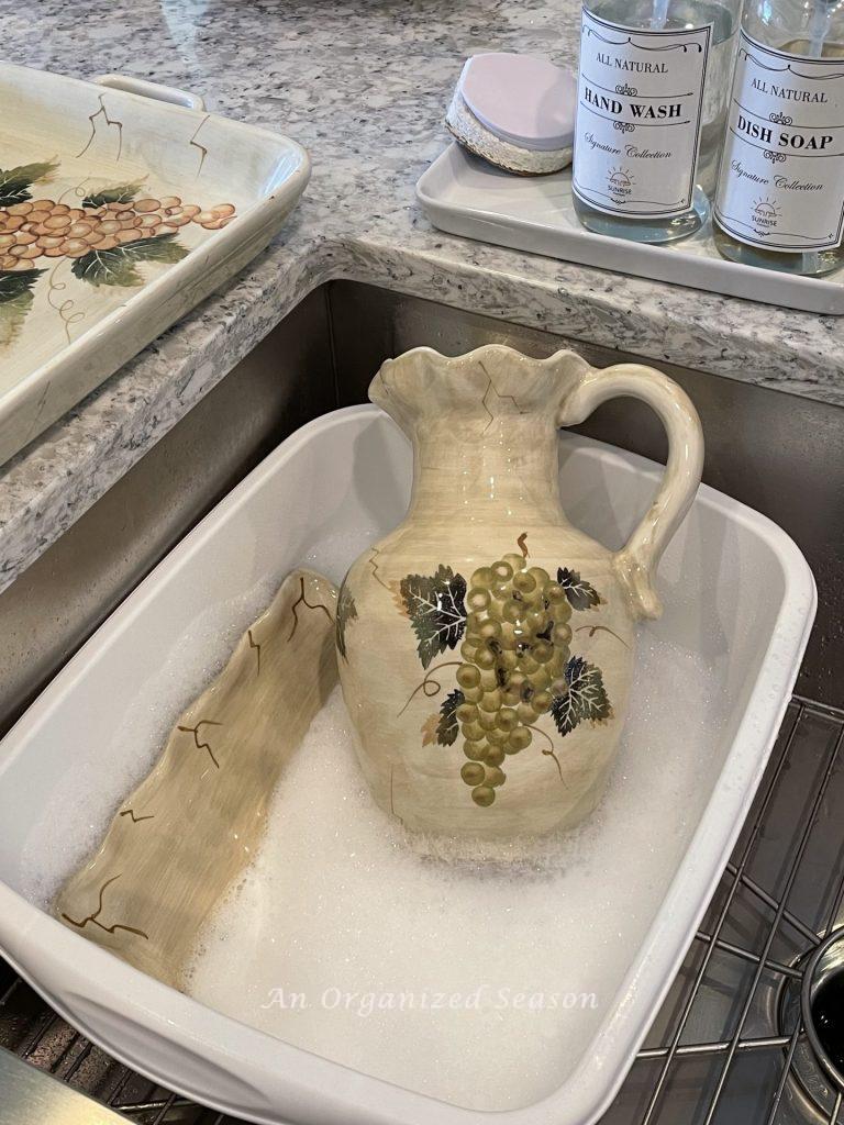 A pitcher being washed in soapy water, the second step to to transform old ceramic items with spray paint!