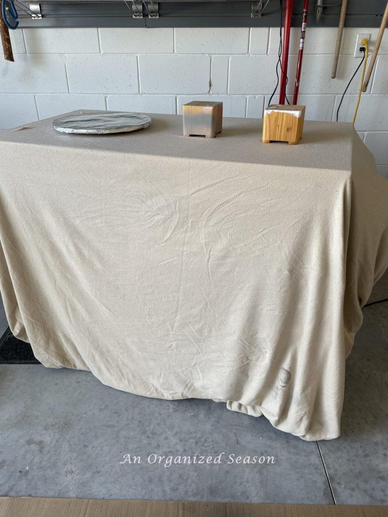Table covered in a sheet with a lazy Susan used to transform old ceramic items with spray paint!