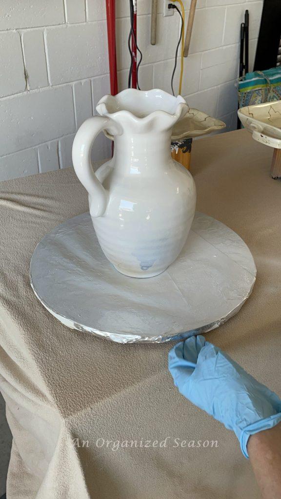 A pitcher being spray painted on a lazy Susan, the third step to to transform old ceramic items with spray paint!