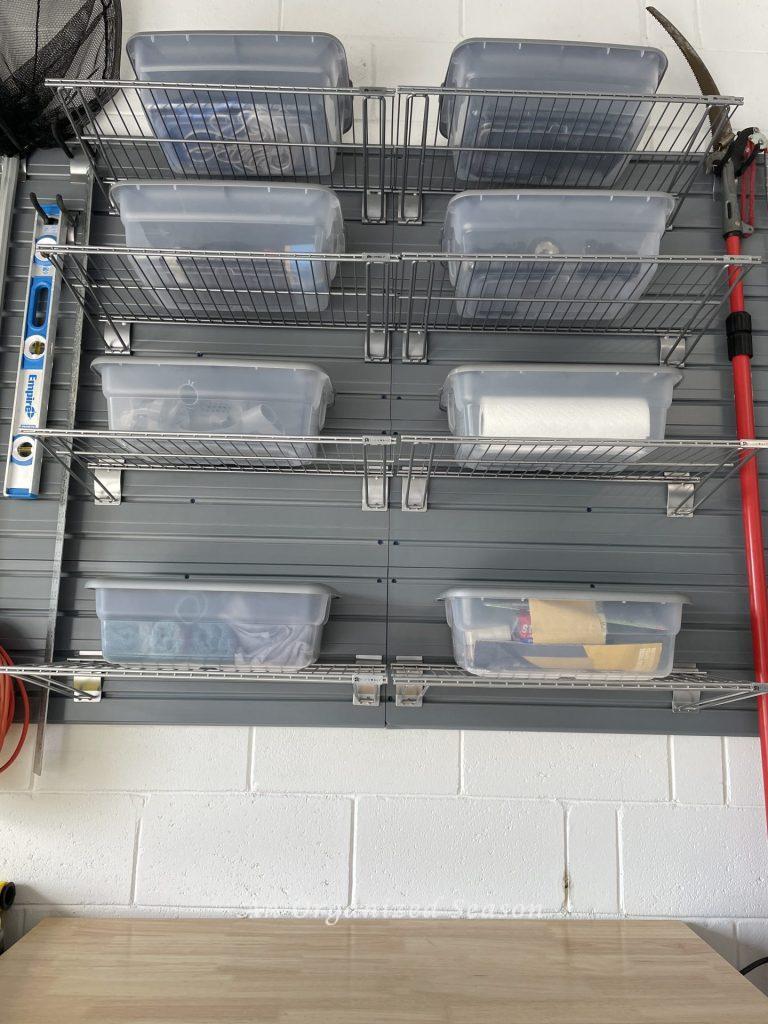 Wire shelves on a garage wall organizer holding clear plastic tubs.  Showing how to organize a garage into zones.