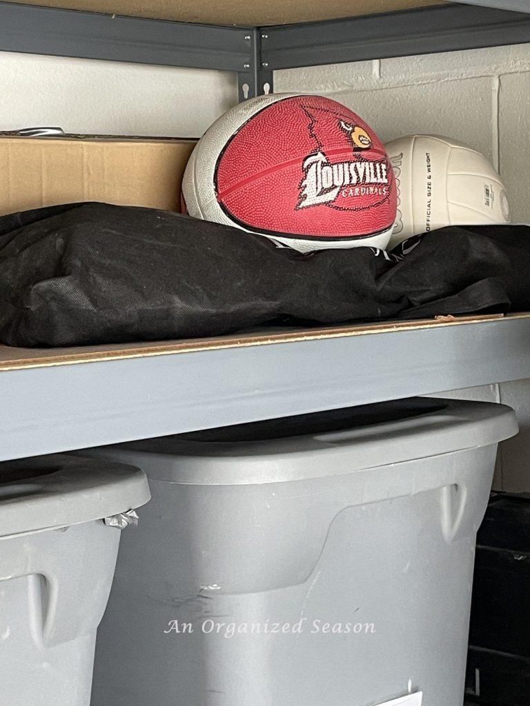 A shelf in a garage storing sports equipment. Showing how to organize a garage into zones.