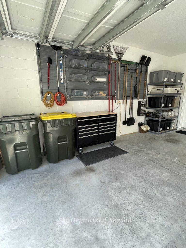 A garage with a storage system on the wall, a storage workbench, and shelves with tubs. Showing how to organize a garage into zones.