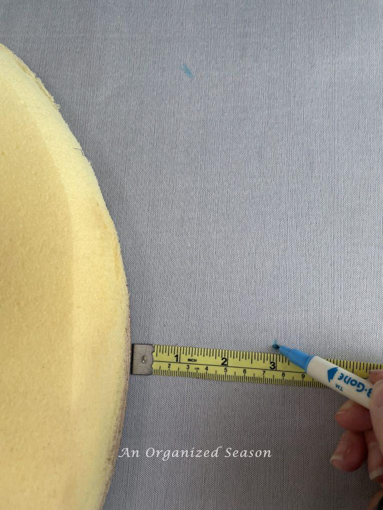 Step five to reupholster seats and stools, is to measure 3 inches around the seat and mark the fabric underneath it.
